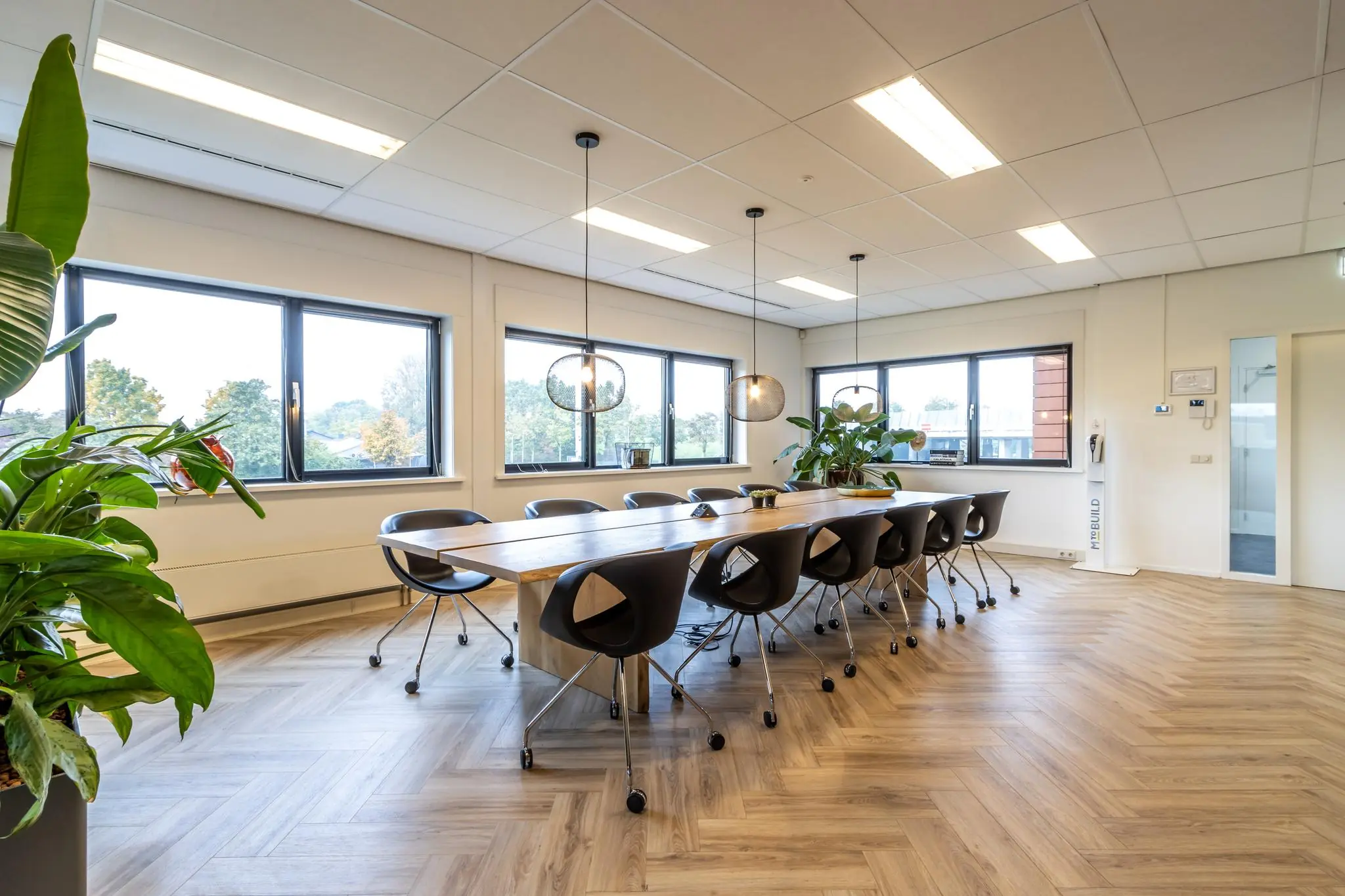 Moderne vergaderruimte aan de Lage Biezenweg met lange houten tafel, zwarte stoelen, grote ramen en hanglampen.